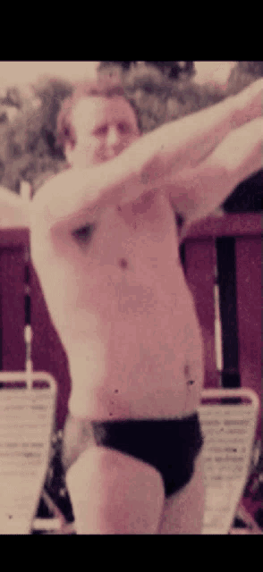 a shirtless man in black swim trunks stretches his arms out
