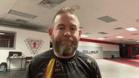 a man with a beard is standing in a gym with a wall that says dollmur