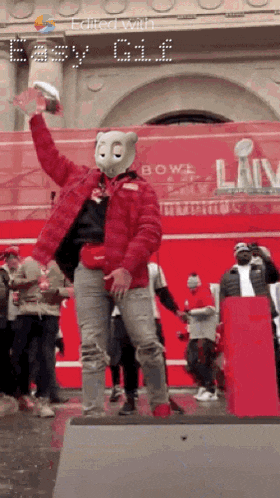 a man wearing a teddy bear mask holds a football in front of a sign that says bowl