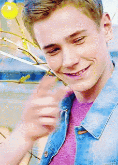 a young man wearing a blue denim jacket and a purple shirt is smiling