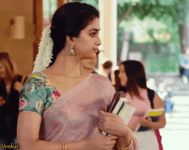 a woman in a pink saree is holding a book and the word venkat is on the bottom left