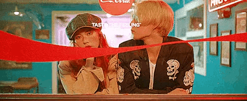 a man and a woman are sitting next to each other in front of a window with a coca cola sign above them .