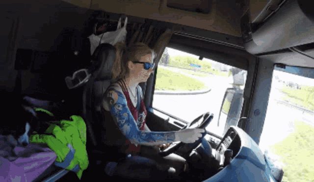 a woman wearing sunglasses is driving a truck with a tattoo on her arm