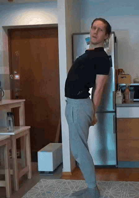 a man in a black shirt and grey pants is standing in front of a refrigerator