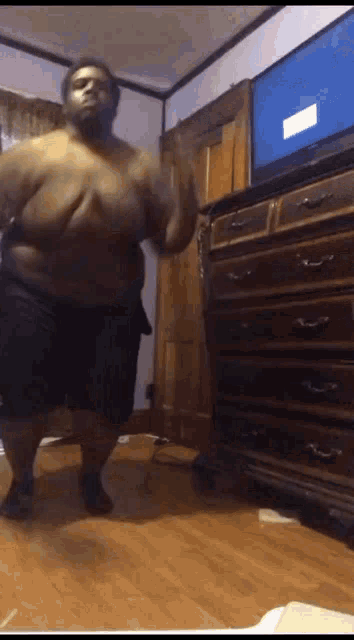 a fat man is dancing in front of a tv in a bedroom