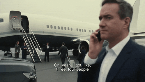 a man talking on a cell phone in front of an airplane with the words oh yeah i got like three four people below him