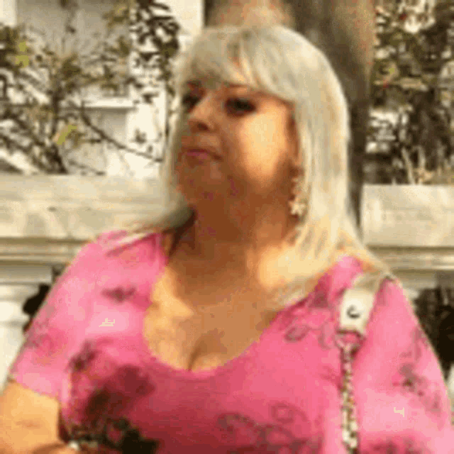 a woman wearing a pink shirt and earrings is standing in front of a building .