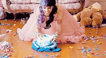 a woman in a pink dress is sitting on the floor holding a cake .