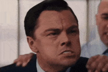 a man in a suit and tie is making a funny face while being hugged by another man .