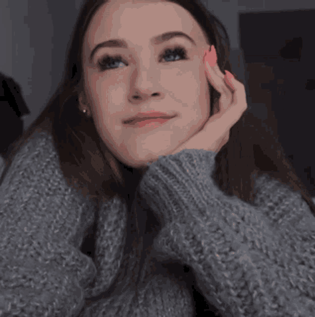 a woman wearing a grey sweater has a pink nail polish on her finger