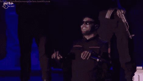 a man wearing sunglasses is singing into a microphone on a stage sponsored by arte