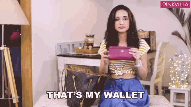 a woman is sitting on a bed holding a purse and the words that 's my wallet