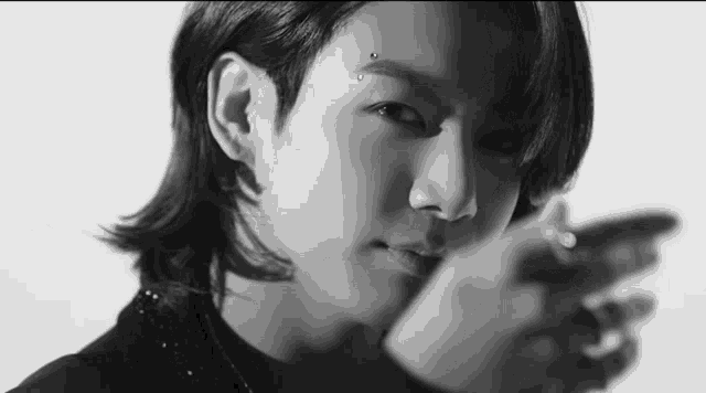 a black and white photo of a young man with long hair and a piercing in his forehead .