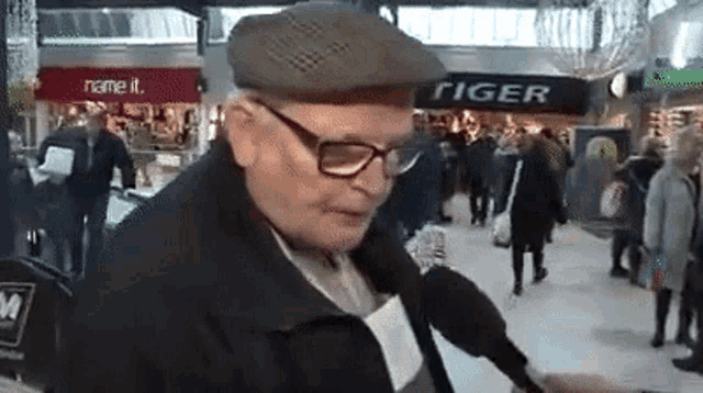 an older man wearing glasses and a hat is standing in front of a store called tiger