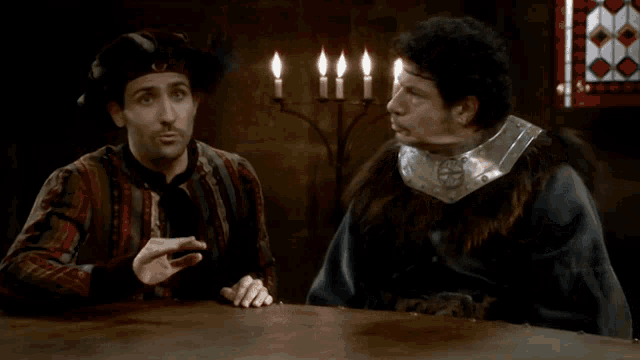 two men are sitting at a table with lit candles in the background