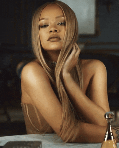 a woman with long blonde hair is sitting in front of a bottle of perfume