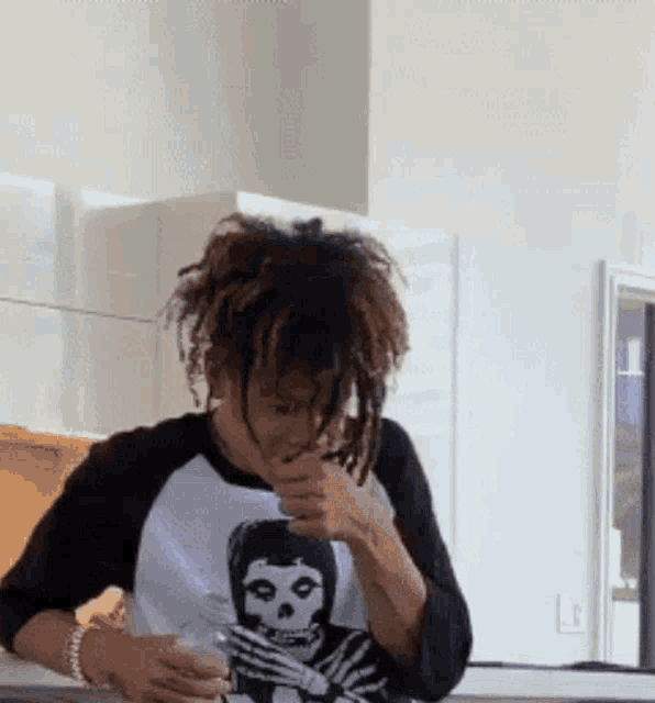a man wearing a shirt with a skeleton on it is drinking from a glass