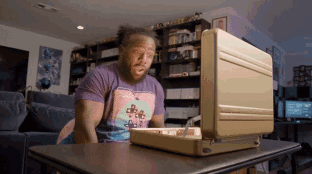 a man sitting at a table with a briefcase in front of him and a shirt that says be a saint