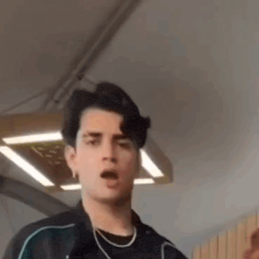 a young man in a black jacket is making a funny face in a room .