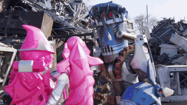 a group of pink and blue robots standing in front of a pile of scrap metal