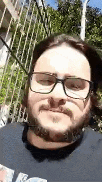a man with glasses and a beard is wearing a black shirt and a hat .