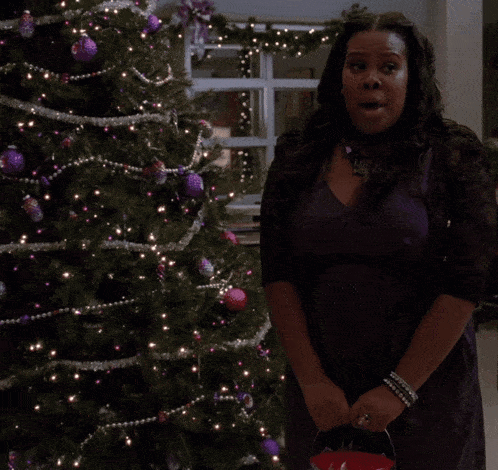 a woman standing in front of a christmas tree