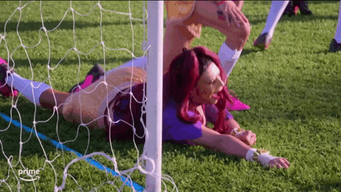a woman with red hair is laying on the grass in front of a soccer net .