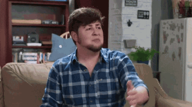 a man in a plaid shirt is sitting on a couch in front of a sign that says your home