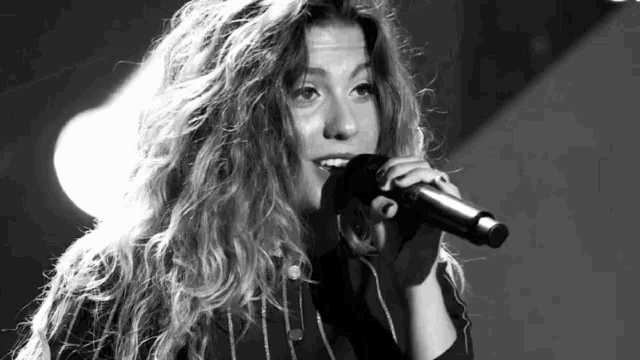 a woman singing into a microphone with a striped shirt on