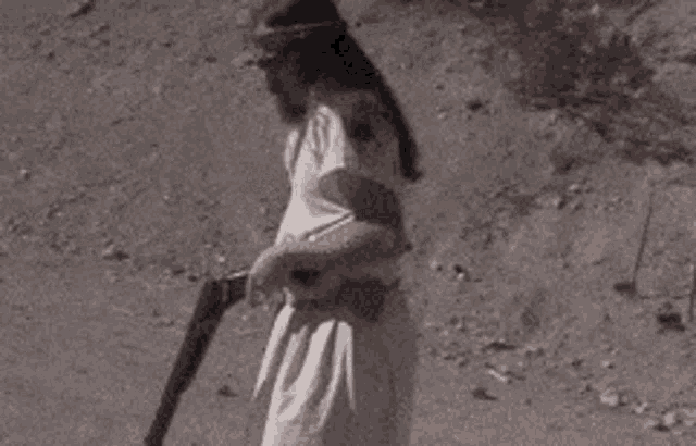 a woman in a white dress is holding a gun in a desert .