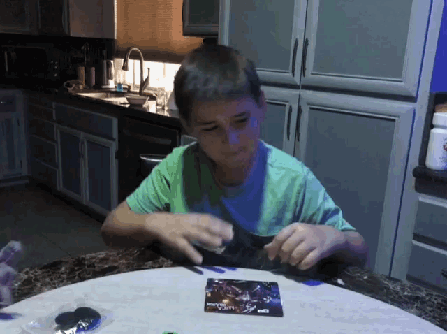 a young boy in a green shirt sits at a table with a card that says ' avengers ' on it