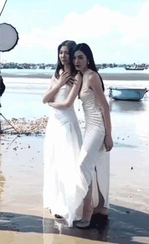 two women in white dresses are posing for a picture on a beach