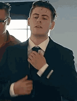 a man in a suit and tie is adjusting his tie while standing next to another man .