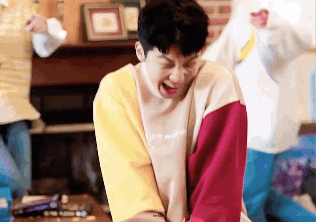a young man in a yellow , white and red sweater is making a funny face in a room .