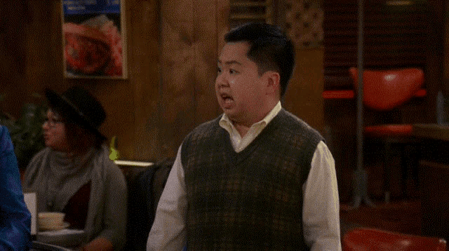 a man in a sweater vest stands in a diner