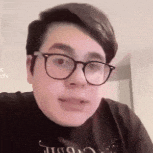 a young man wearing glasses and a black shirt is making a face .