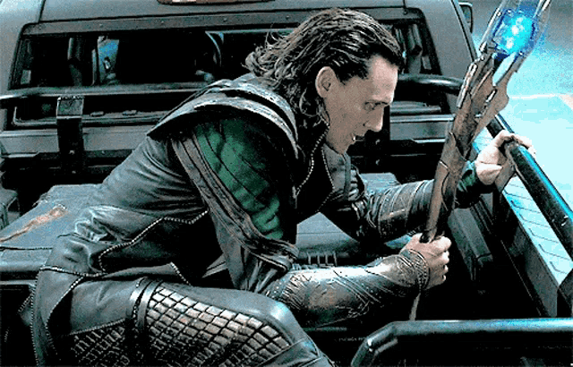 a man in a leather jacket is sitting in the back of a car holding a sword .