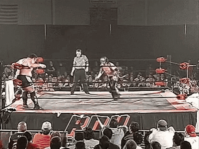 two men are wrestling in a wrestling ring with a referee in the background .