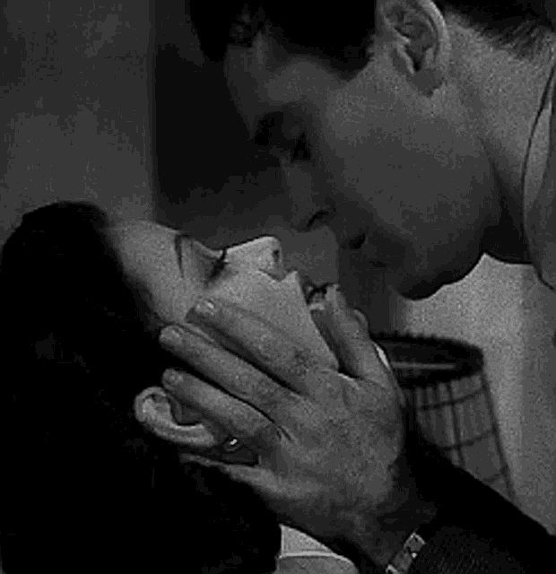 a black and white photo of a man kissing a woman on the cheek .