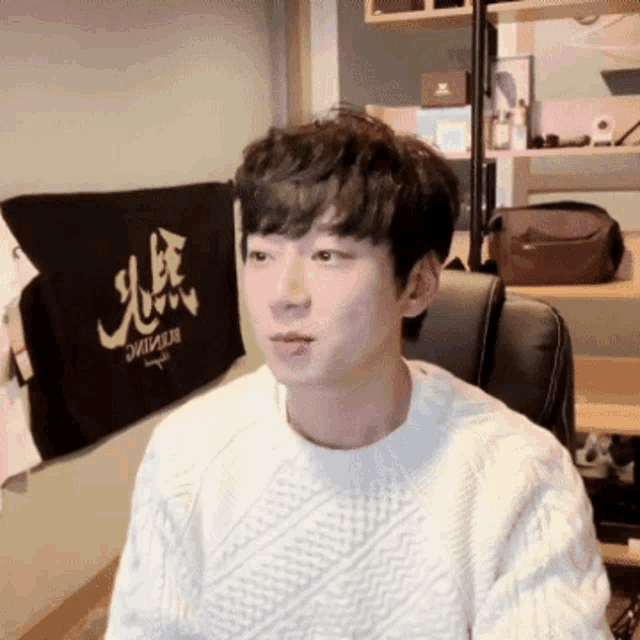 a young man wearing a white sweater is sitting in front of a black towel that says " resilience "