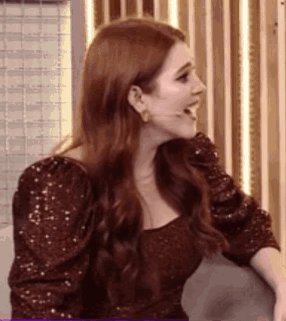 a woman with red hair is wearing a sequined dress and earrings while sitting in a chair .