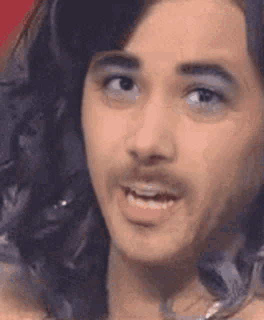 a man with long hair and a beard is wearing makeup and making a funny face .