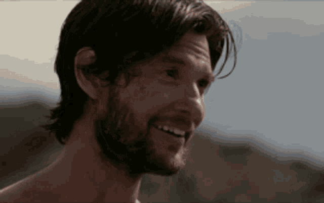 a shirtless man with a beard is smiling and looking to the side
