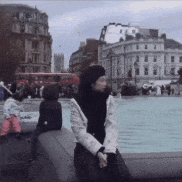 a woman in a black beret sits on a ledge in front of a fountain