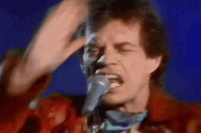 a close up of a man singing into a microphone while scratching his head .