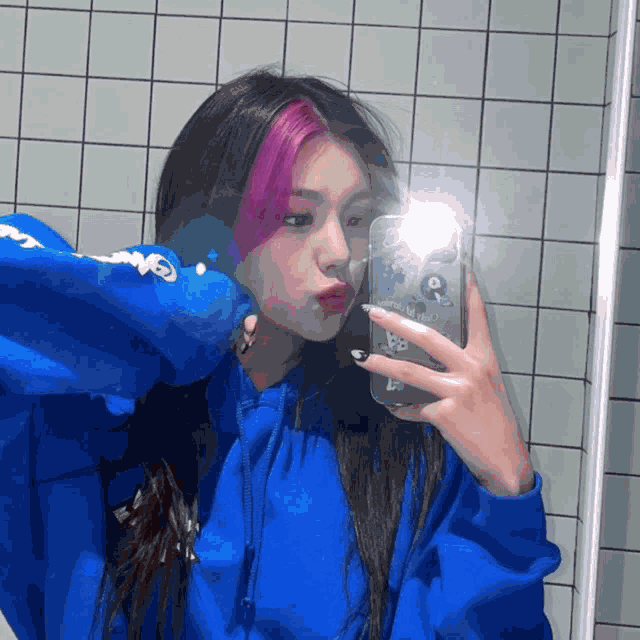 a girl in a blue hoodie is taking a picture of herself in the mirror