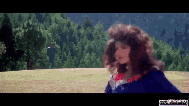 a woman in a blue dress is standing in a field with a man in a blue jacket behind her .