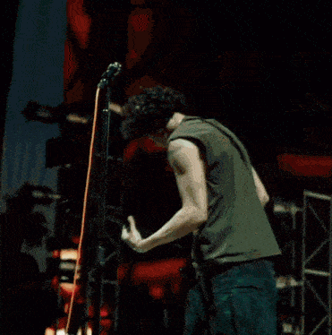 a man in a green tank top is playing a guitar in front of a microphone