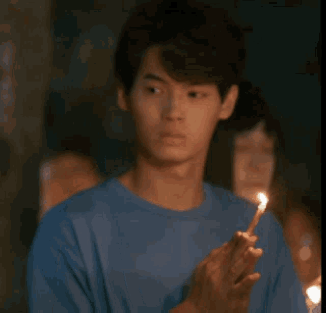 a man in a blue shirt is holding a lit match and says hey in thai