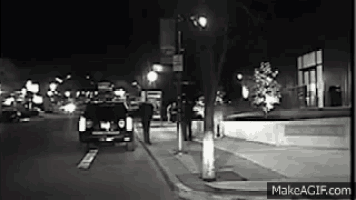 a black and white photo of a car driving down a city street at night